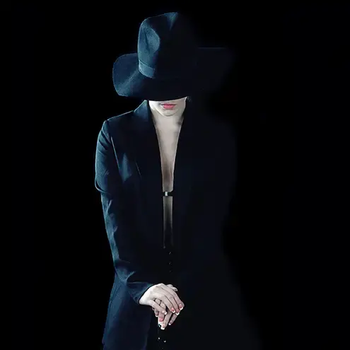 A low key high fashion photograph of a girl wearing a black jacket and black hat against a black background