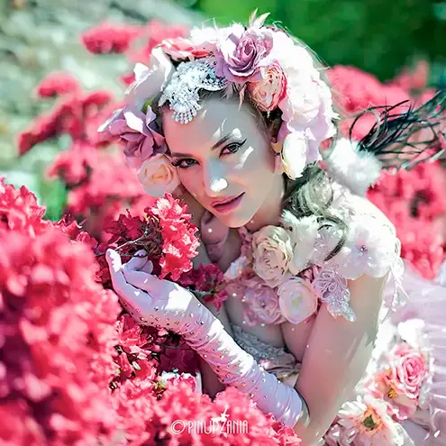 A burlesque dancer in a flower headdress posing amongst roses