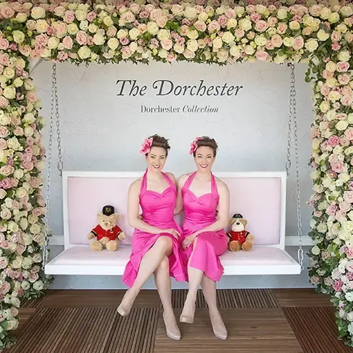 Twin sisters in pink dresses under a flower arch