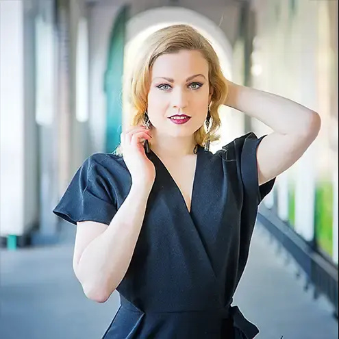 A blonde model in a black dress posing outside, high fashion, editorial