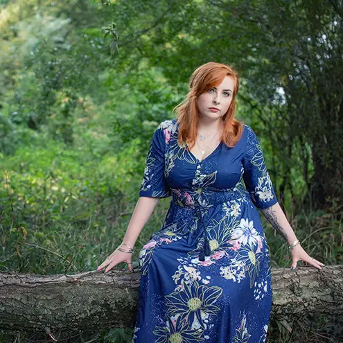 A redhaired model in a blue dress sitting on a tree